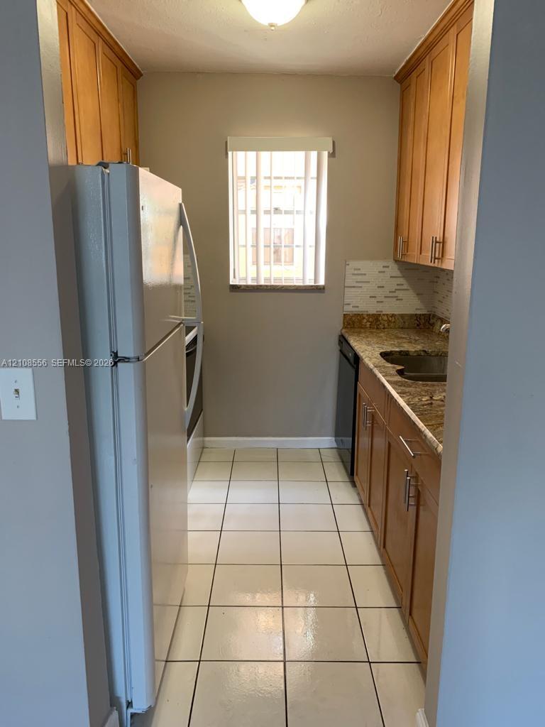 Kitchen featuring natural wood cabinetry, stone countertops, tiled backsplash, large-format tile flooring, and a window Kitchen featuring natural wood cabinetry, stone countertops, tiled backsplash, large-format tile flooring, and a window