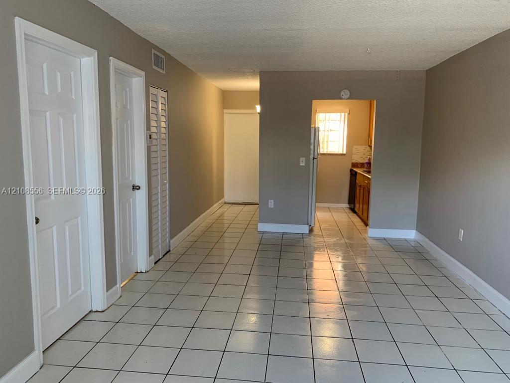Neutral-toned interior featuring ceramic tile flooring, solid-core interior doors, louvered closet doors, and recessed kitchen cabinetry Neutral-toned interior featuring ceramic tile flooring, solid-core interior doors, louvered closet doors, and recessed kitchen cabinetry