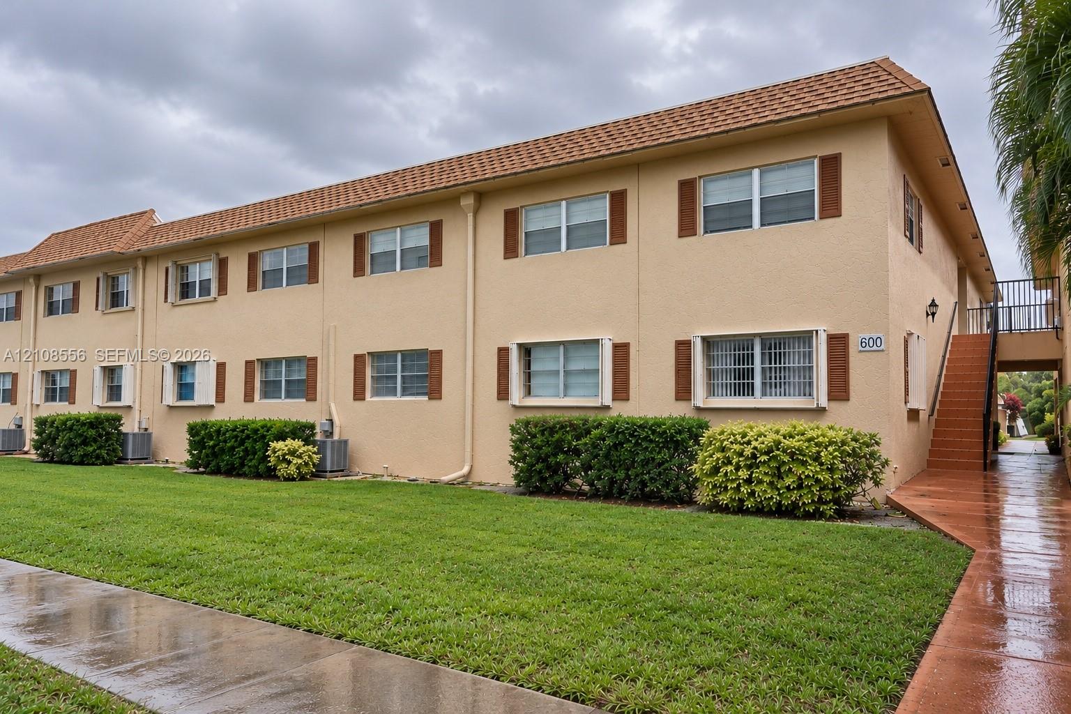 Two-story exterior featuring a stucco facade, clay-tile roof, shuttered windows, and external staircase Two-story exterior featuring a stucco facade, clay-tile roof, shuttered windows, and external staircase