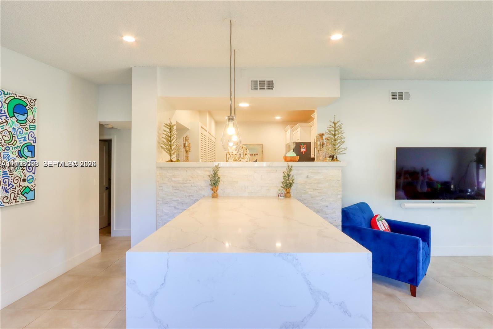 Kitchen island featuring a waterfall-edge countertop, stone-textured facade, and pendant lighting