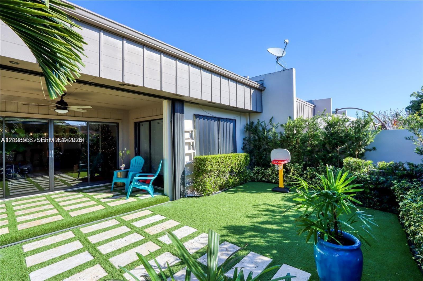 Private patio featuring synthetic turf, paver hardscaping, integrated ceiling fan, and perimeter hedge landscaping