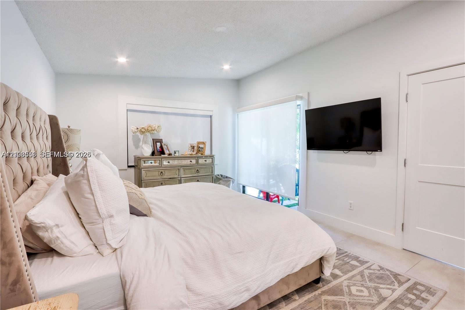 Neutral-toned interior featuring recessed ceiling lighting, light-colored tile flooring, and a sliding glass door with roller shade