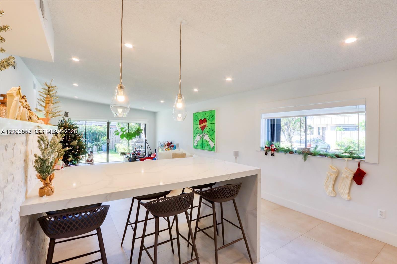 Waterfall island with stone-surface countertop, recessed ceiling lighting, clear glass pendant fixtures, and large-format tile flooring