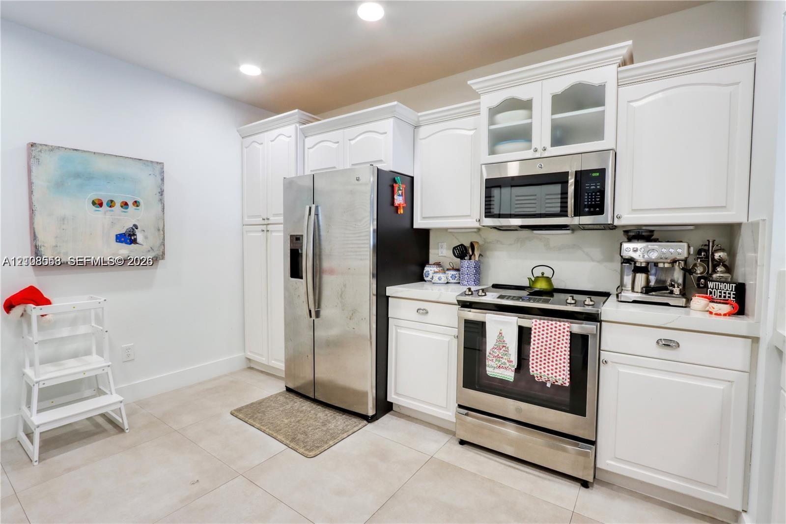 Kitchen featuring white cabinetry with glass-panel upper doors, stainless steel refrigerator, stainless steel range with overhead microwave, and stone-finish flooring