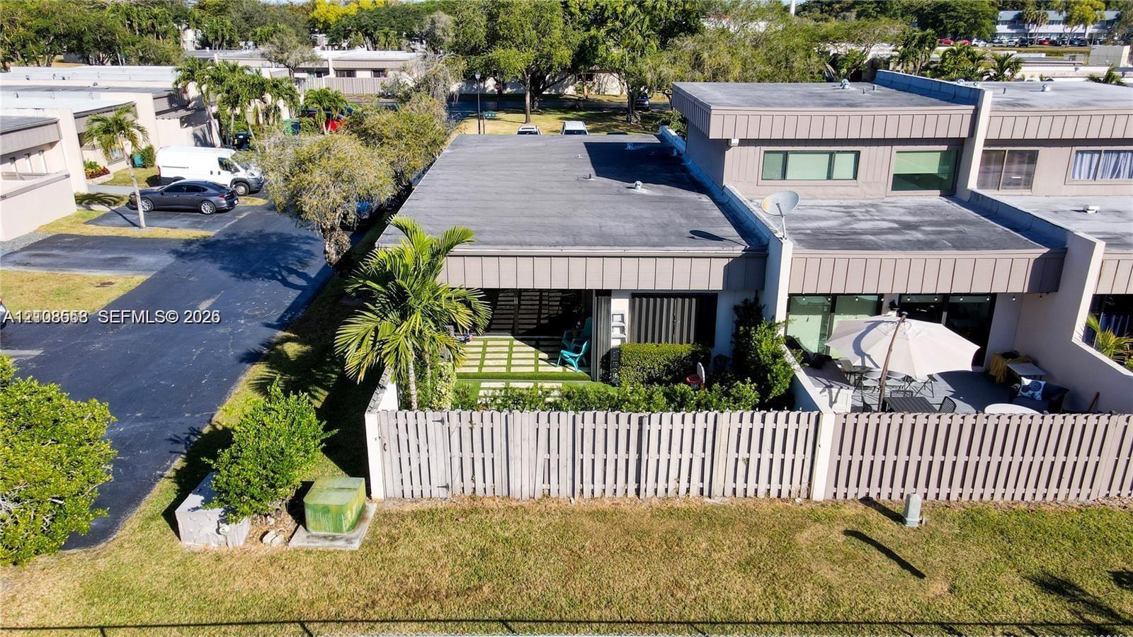 Multi-level exterior featuring a flat roofline, fenced patio area, ground-level paved terrace, and manicured landscaping