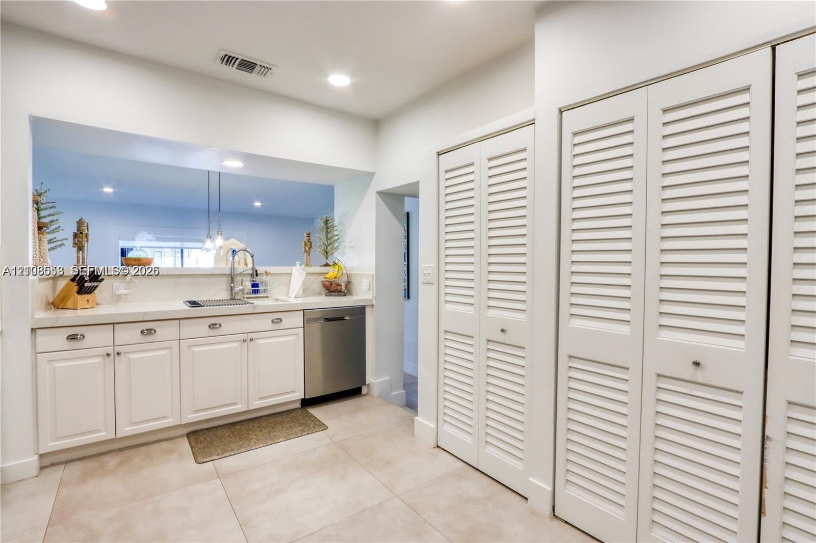 White cabinetry with metal hardware, light-colored solid surface countertops, stainless steel dishwasher, and floor-to-ceiling louvered closet doors