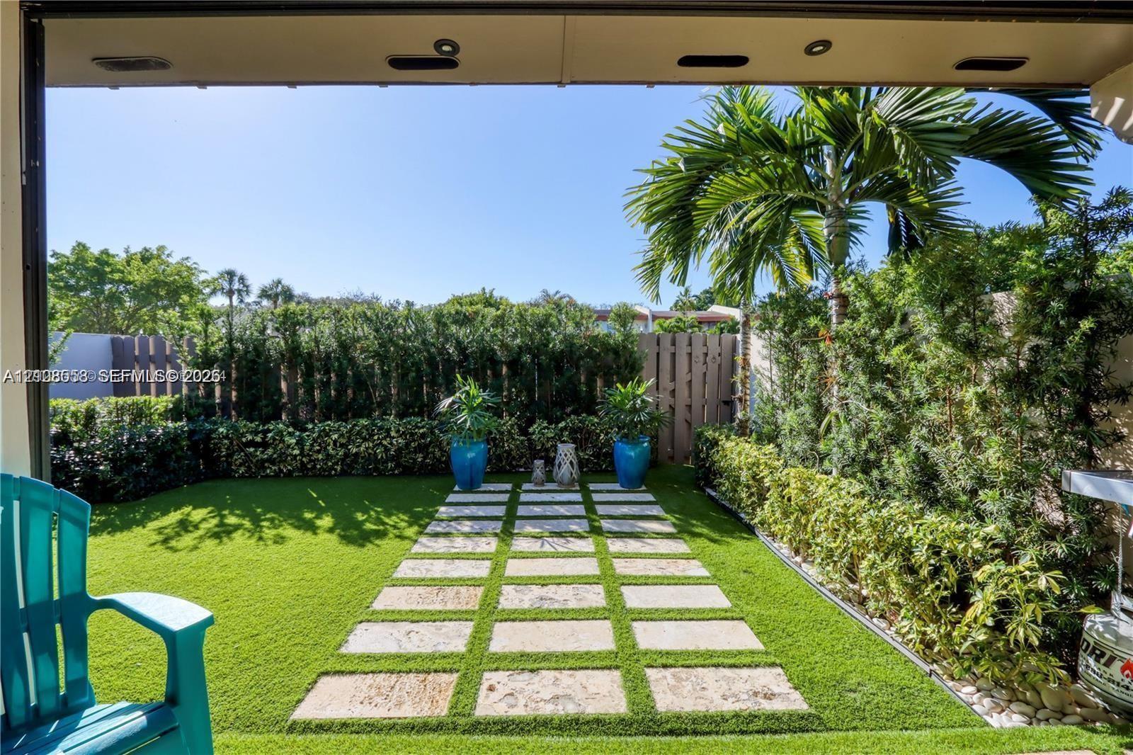 Enclosed backyard featuring synthetic turf, stone paver pathway, mature perimeter hedge privacy screen, and recessed soffit lighting