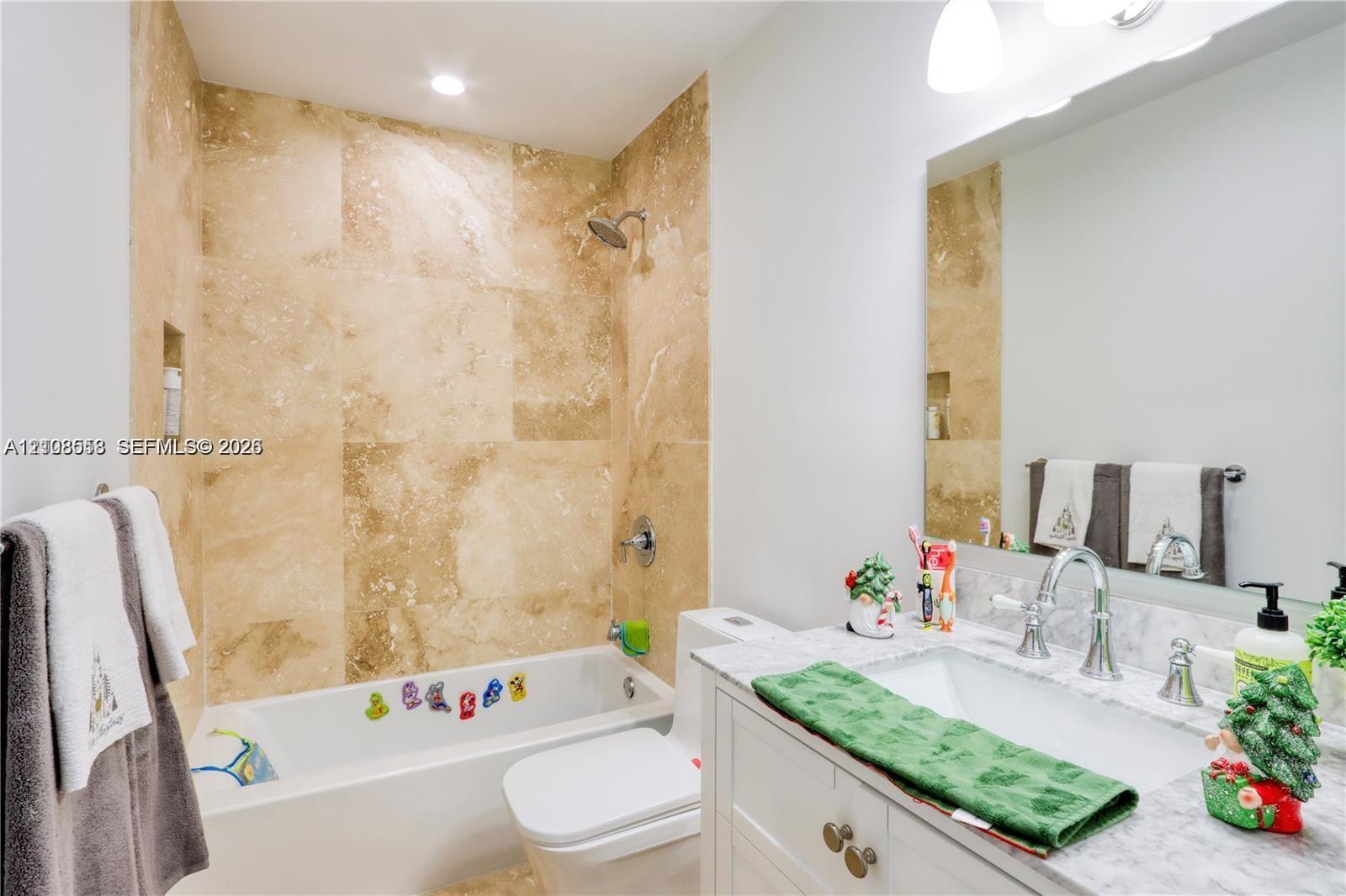 Bathroom featuring large-format natural stone wall tile, an undermount rectangular sink, a light-toned stone vanity countertop, white cabinetry with metallic hardware, and a large wall-mounted mirror