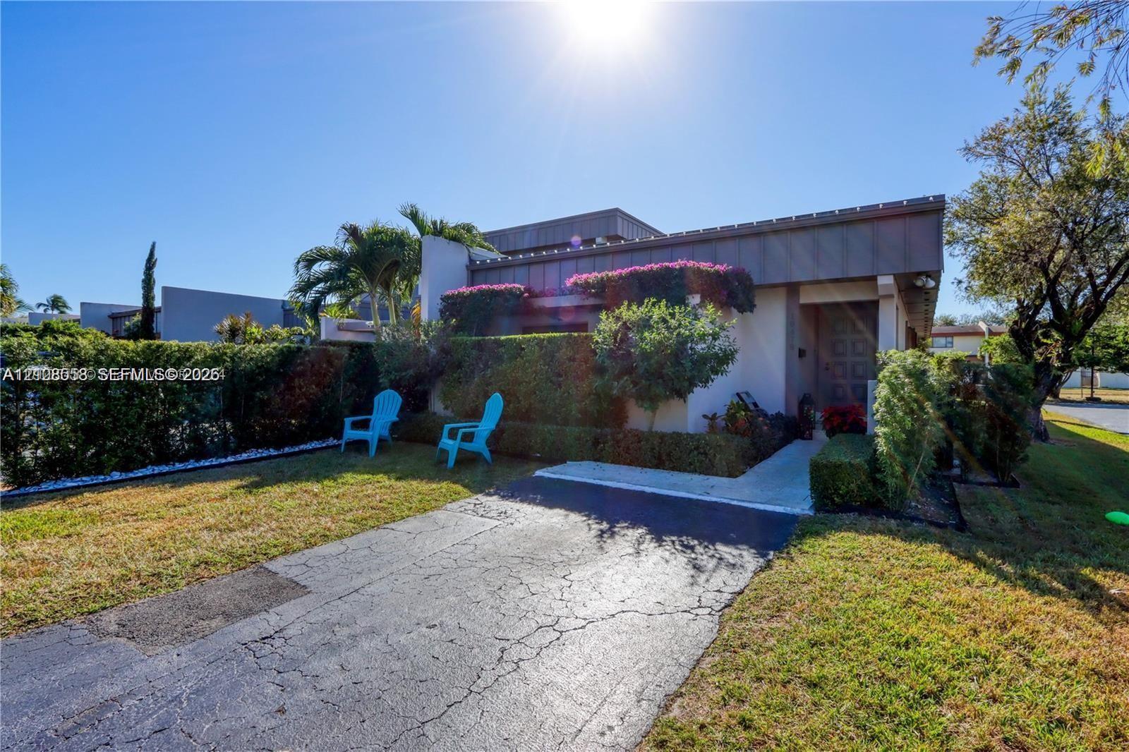 Single-story residence featuring a flat roofline, asphalt driveway, concrete entry walkway, and mature landscaping