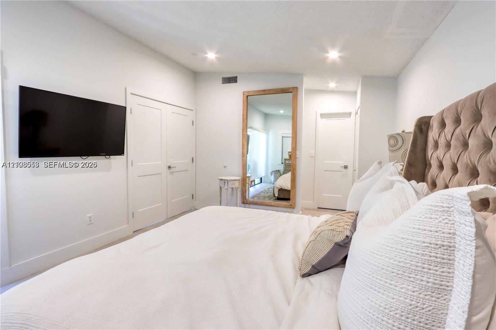 Bedroom interior featuring recessed lighting, dual-panel closet doors, and smooth, neutral-toned walls