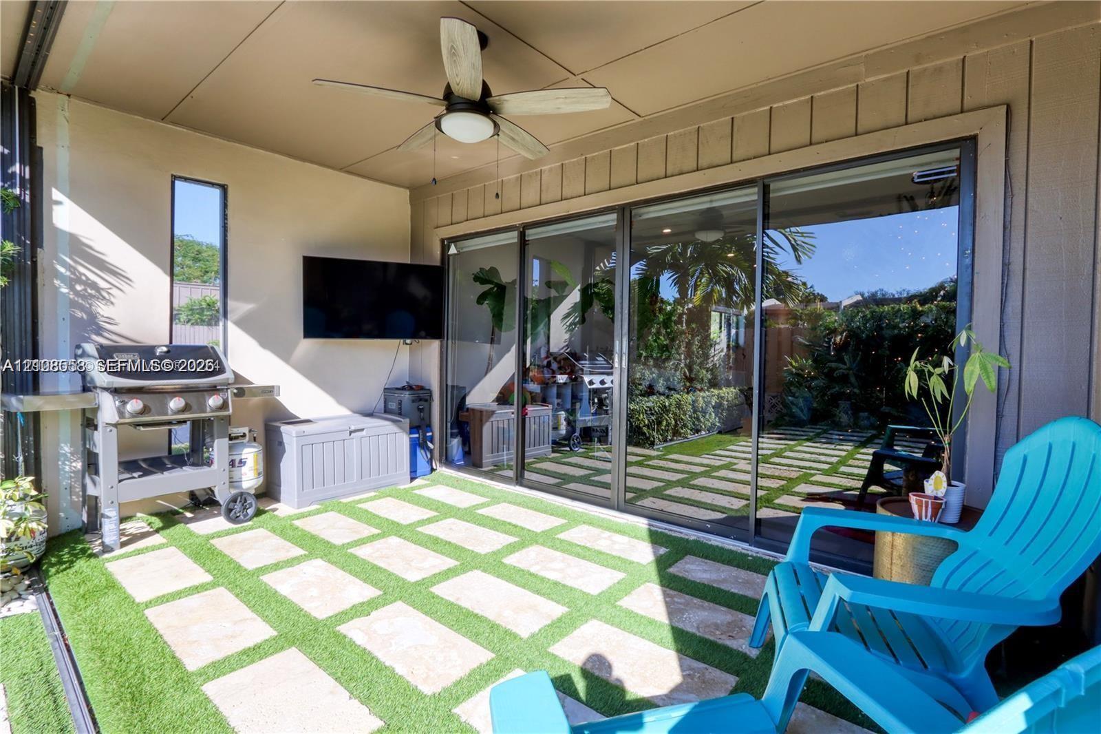 Covered patio featuring artificial turf, stone pavers, ceiling-mounted fan, and sliding glass wall system