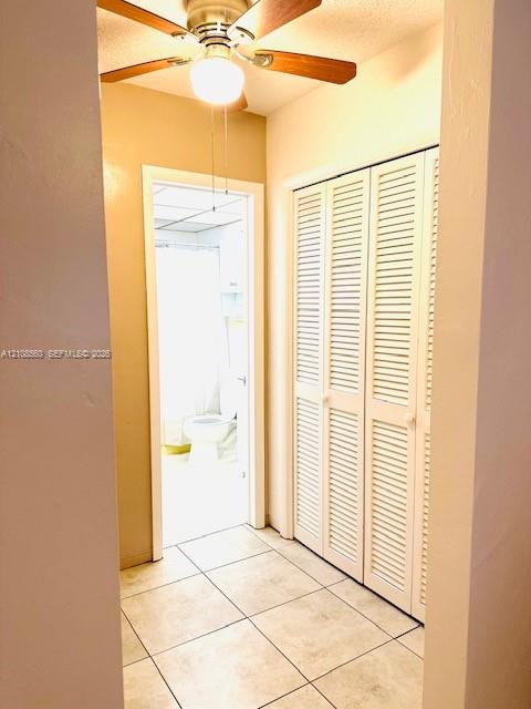 Hallway featuring tile flooring, louvered bi-fold closet doors, and a ceiling-mounted fan with integrated lighting