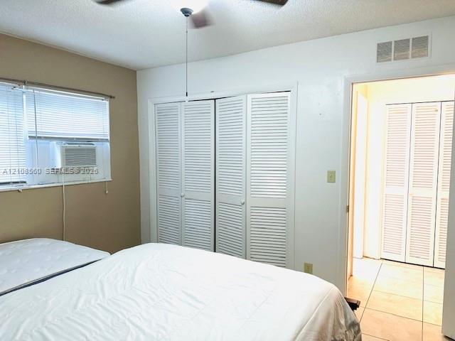 Room featuring dual bifold louvered closet doors, window with integrated air conditioning unit, and ceramic tile flooring