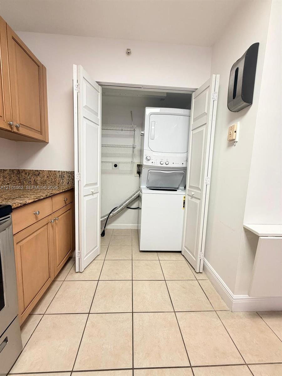 Laundry area featuring a stacked washer and dryer, tile flooring, built-in cabinetry, and stone-finish countertop