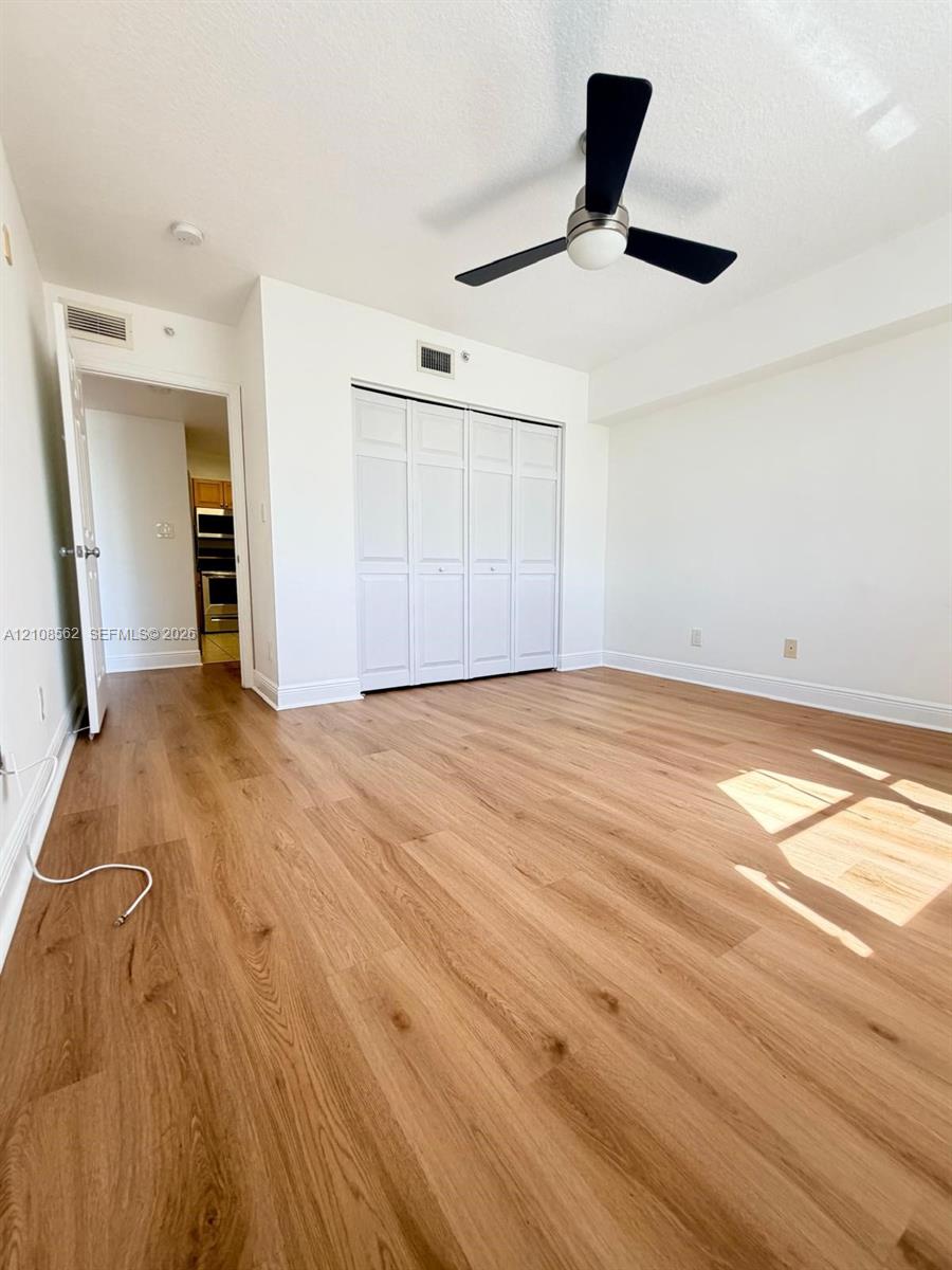 Room featuring wood-finish flooring, a ceiling fan with matte black blades, and a closet with bifold doors