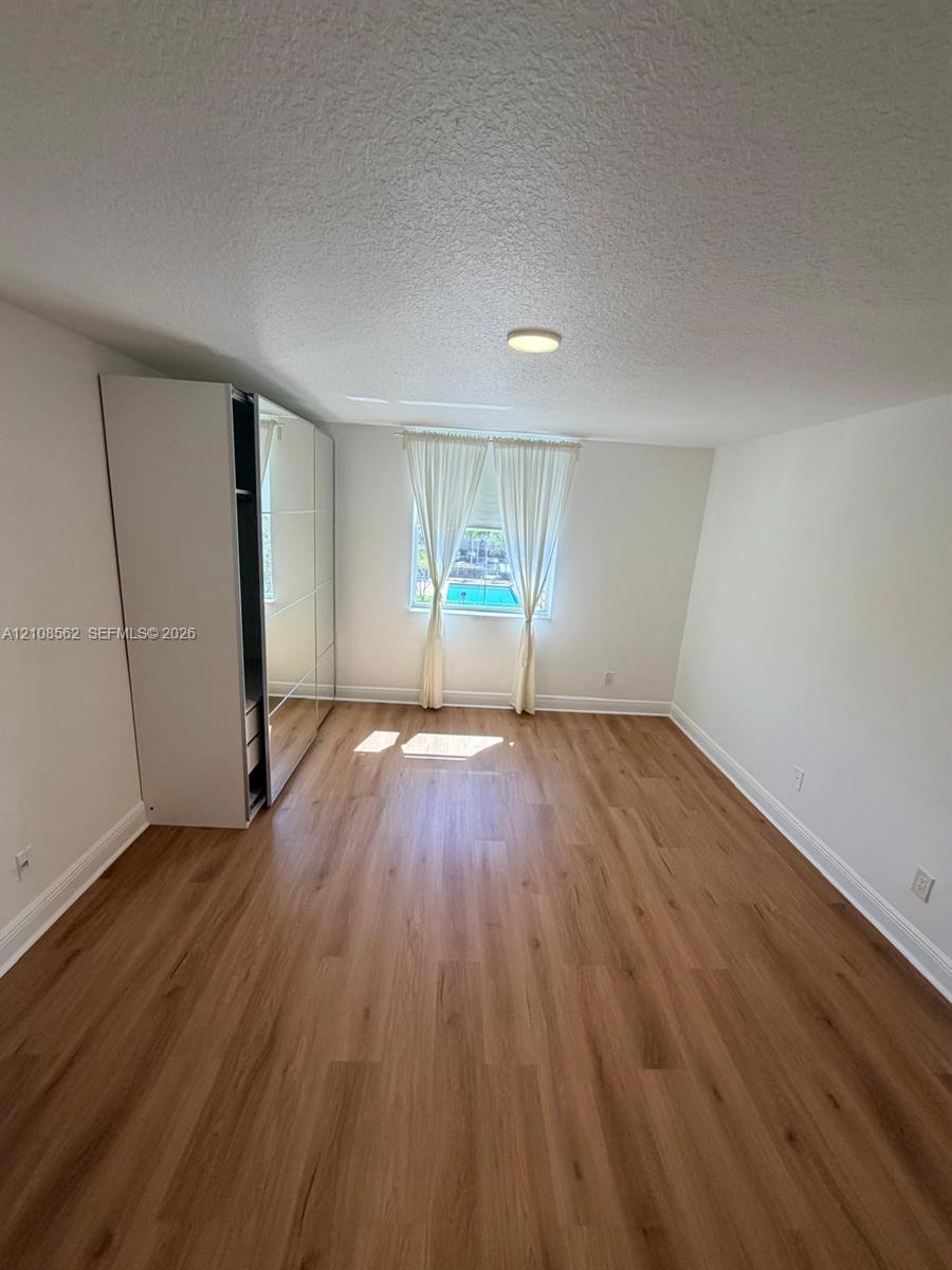 Neutral interior space featuring wood-finish flooring, a built-in full-height wardrobe with mirrored sliding doors, and a central ceiling-mounted light fixture