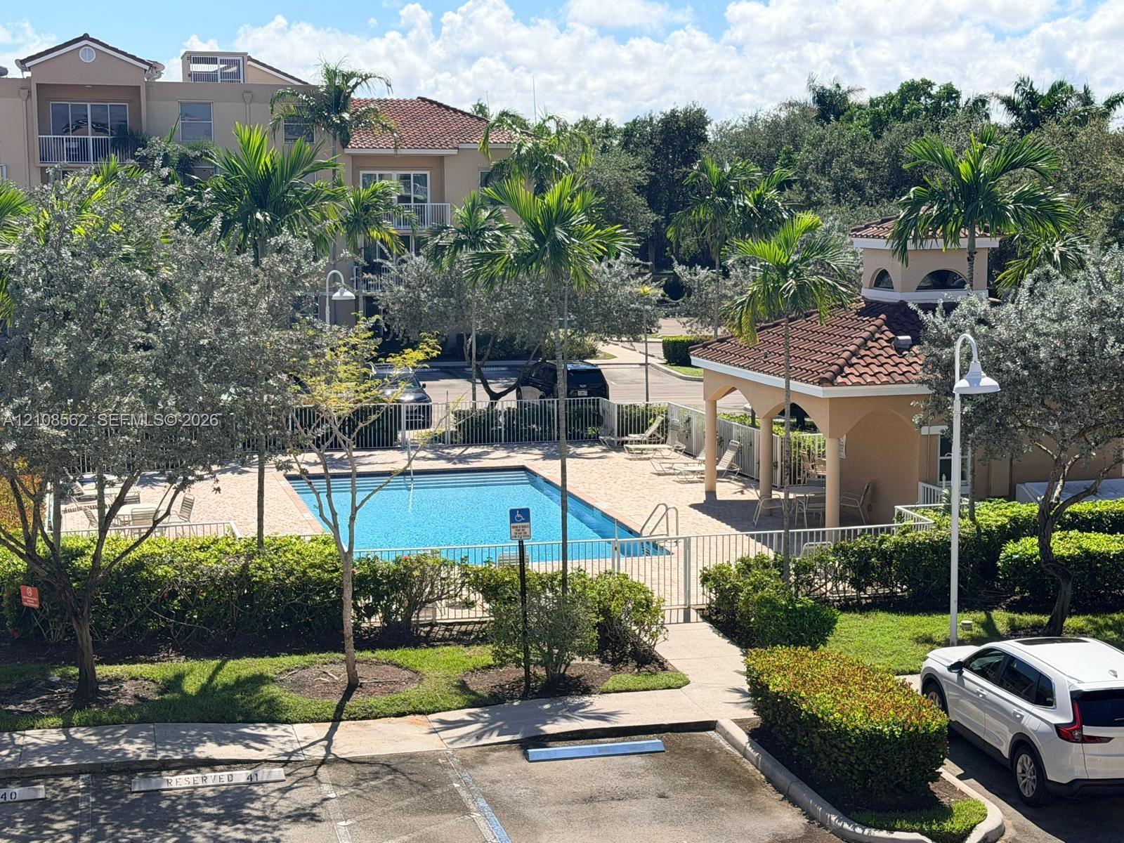 Outdoor swimming pool featuring a tile-roofed cabana and paved deck surrounded by mature palm trees and manicured landscaping