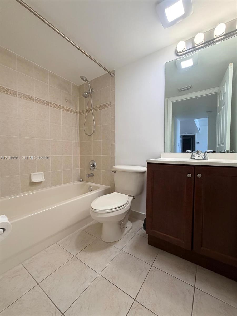 Bathroom featuring a tub-shower combination with ceramic tile surround, dark wood-finish cabinetry, a white countertop, and ceramic floor tiling