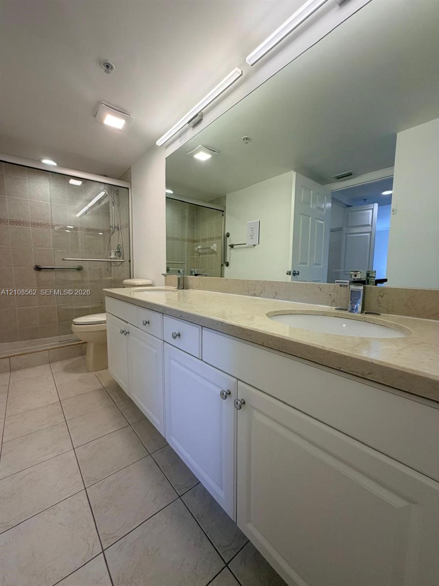 Double vanity featuring white cabinetry, stone-finish countertops, dual integrated sinks, and a full-width wall mirror, complemented by a walk-in shower with tile surround and glass enclosure