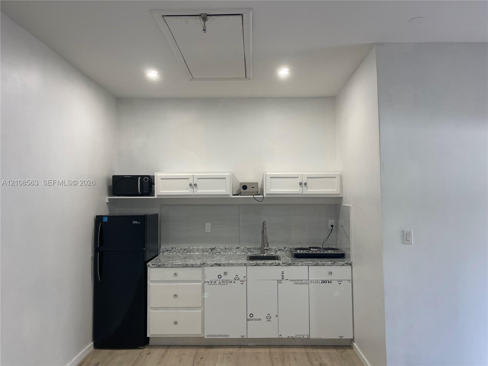 Kitchenette featuring white shaker-style cabinetry, stone-finish countertops, an undermount stainless steel sink with a high-arch faucet, and wood-finish flooring