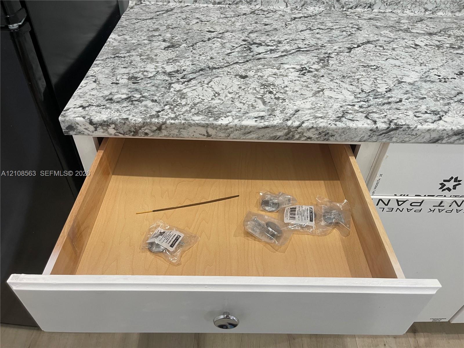 Custom-crafted cabinetry featuring a white shaker-style drawer front, polished metallic hardware, and natural wood drawer box construction, accented by stone-finish countertops