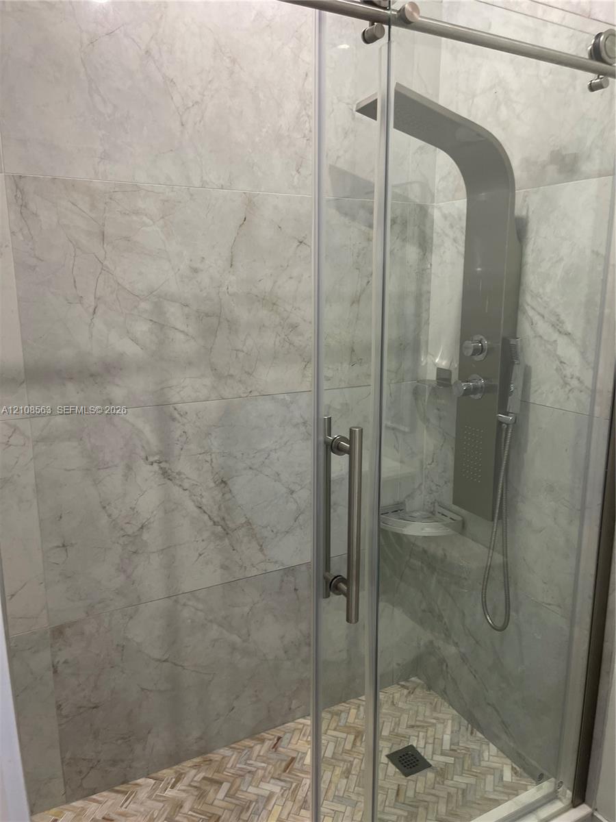 Walk-in shower featuring large-format stone-pattern wall tile, herringbone-pattern stone tile flooring, a glass sliding door with metal hardware, and a multi-function shower panel system