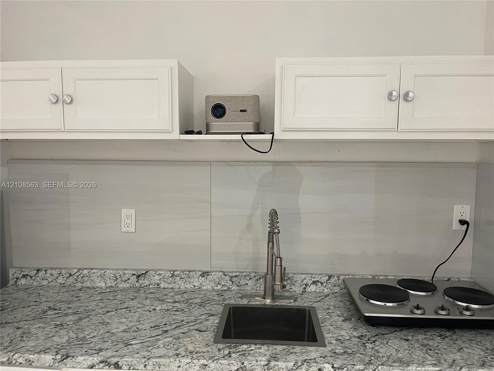Kitchen area featuring stone-patterned countertops, a stainless steel undermount sink, a pull-down high-arch faucet, a smooth-top electric cooktop, and white cabinetry