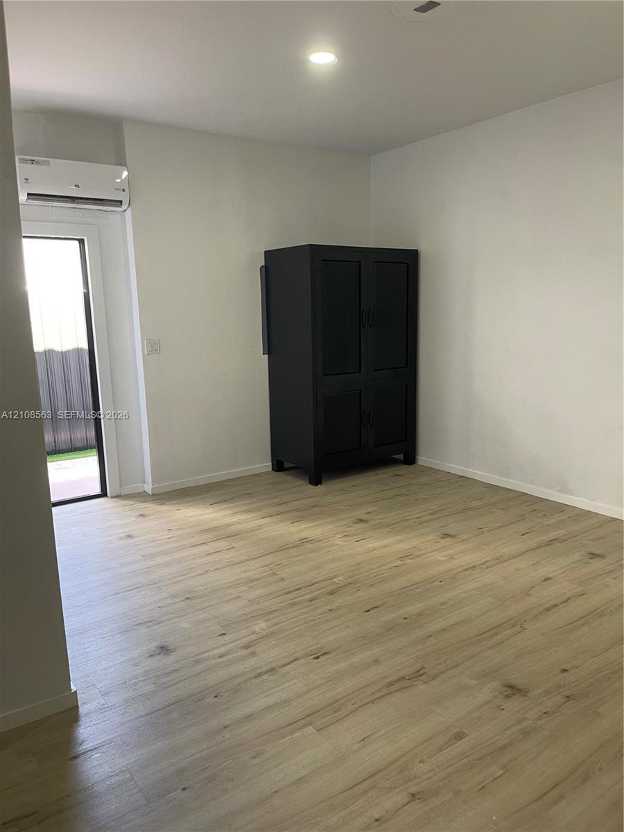 Room featuring wood-finish flooring, recessed lighting, and a wall-mounted ductless climate control unit with access to an exterior entry