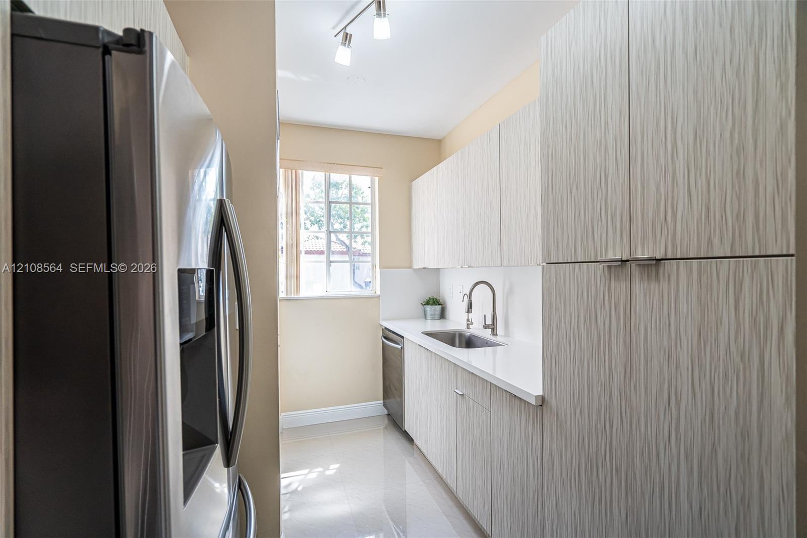 Galley kitchen featuring textured cabinetry, white solid-surface countertops, stainless steel appliances, a high-arc faucet, and track lighting