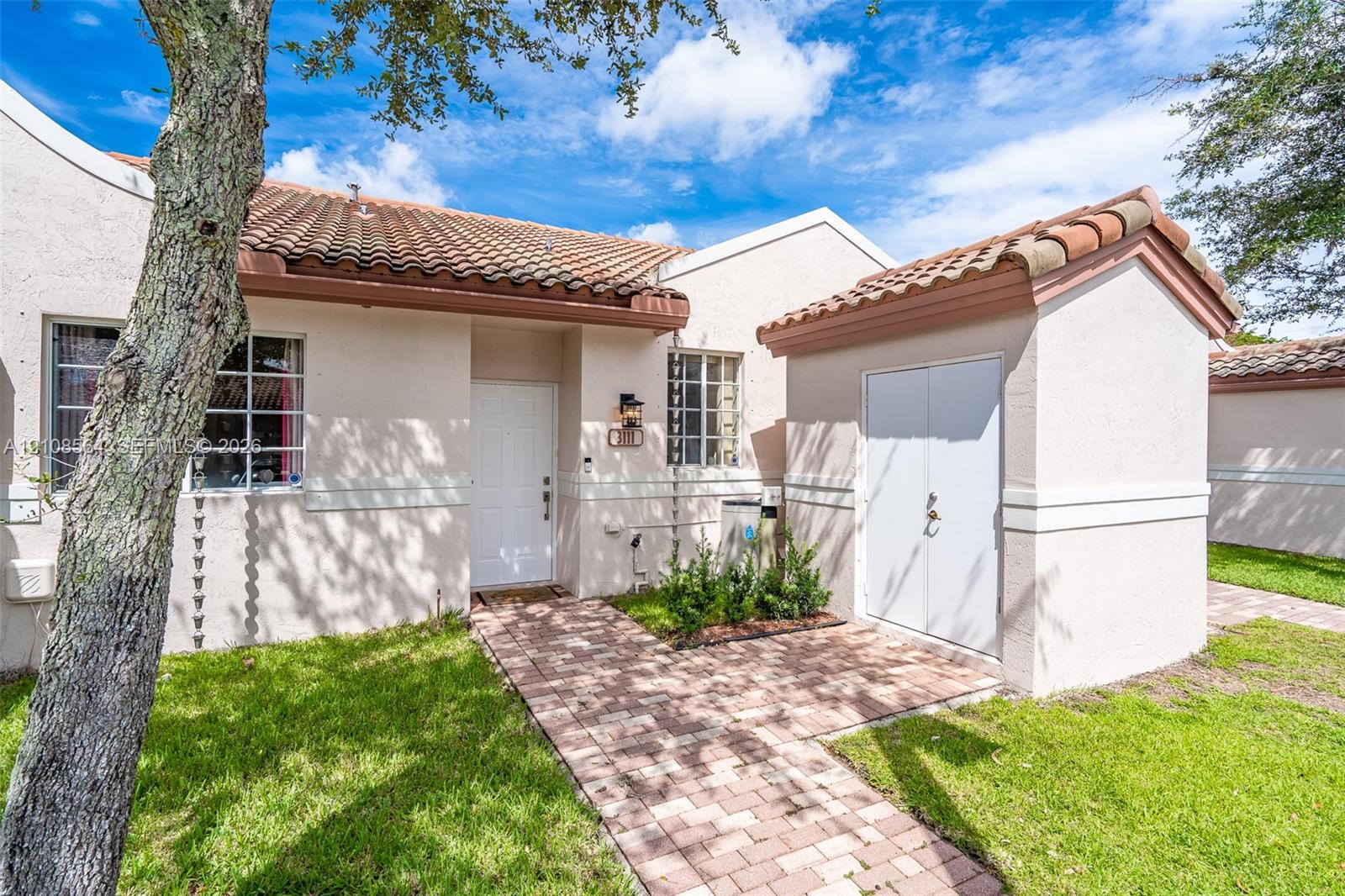 Stucco exterior featuring a clay tile roof, brick paver walkway, white paneled front door, and an attached exterior storage structure Stucco exterior featuring a clay tile roof, brick paver walkway, white paneled front door, and an attached exterior storage structure