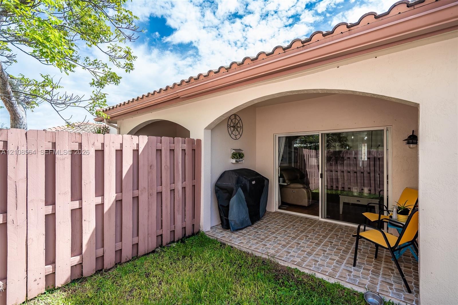 Covered patio featuring stone-finish tile flooring and arched architectural detailing, enclosed by privacy fencing and sliding glass doors