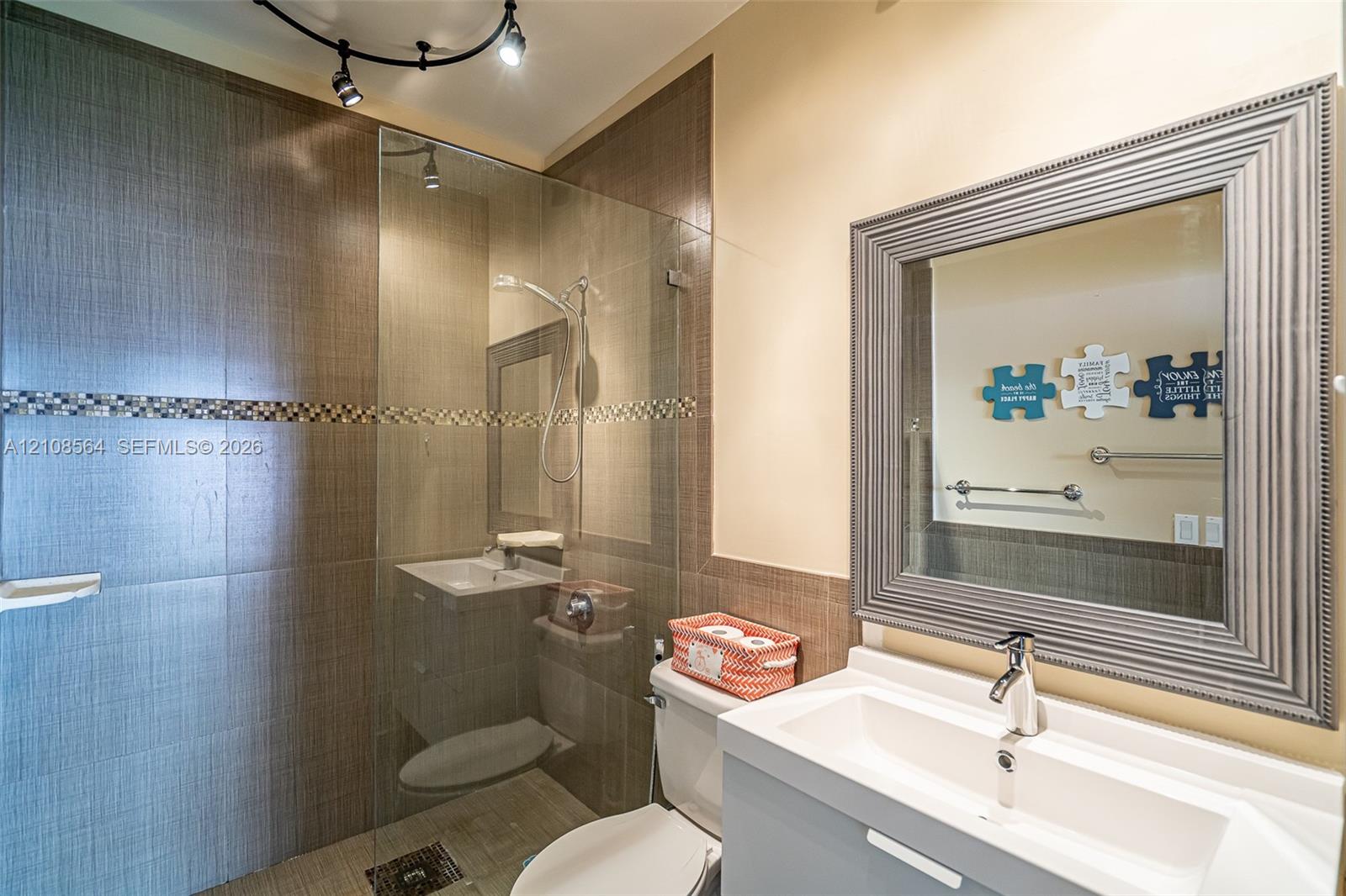 Bathroom featuring a glass-enclosed walk-in shower with floor-to-ceiling textured tile, a decorative mosaic accent border, a floating vanity with a rectangular basin, and a framed mirror