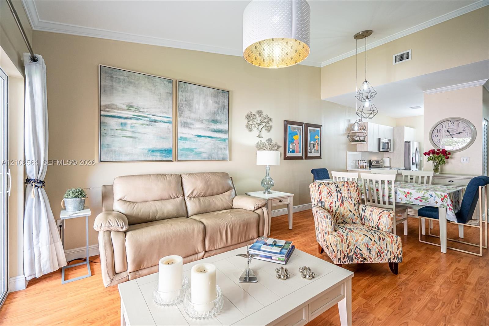 Open-concept interior featuring wood-finish flooring, crown molding, a large drum pendant light, and geometric multi-light fixtures