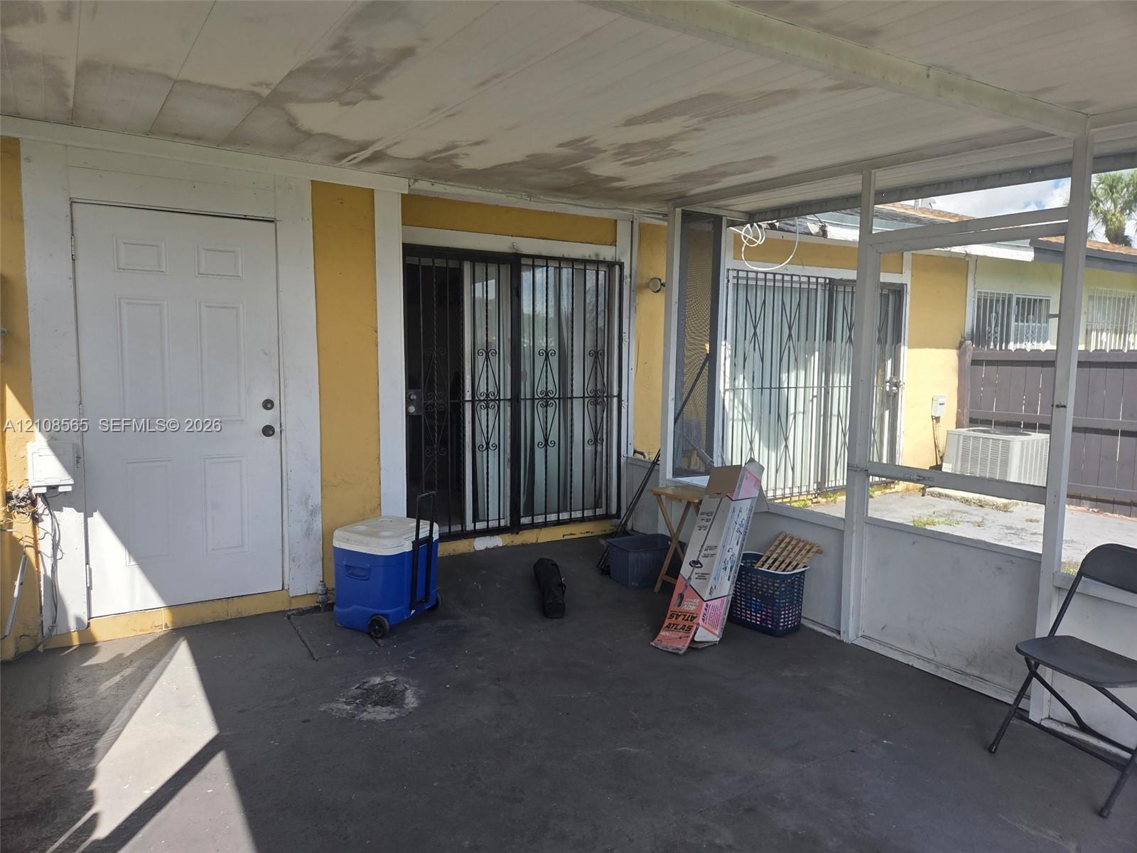 Enclosed patio featuring a concrete floor, metal screening, a solid core entry door, and metal security bars on sliding glass doors