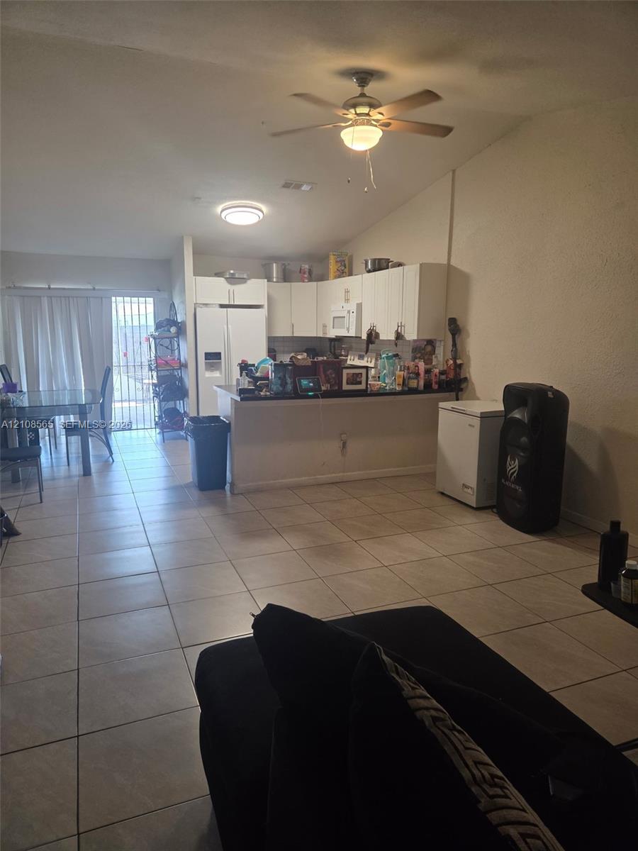 Ceramic tile flooring throughout with white cabinetry, built-in breakfast bar, ceiling fan, and sliding glass door