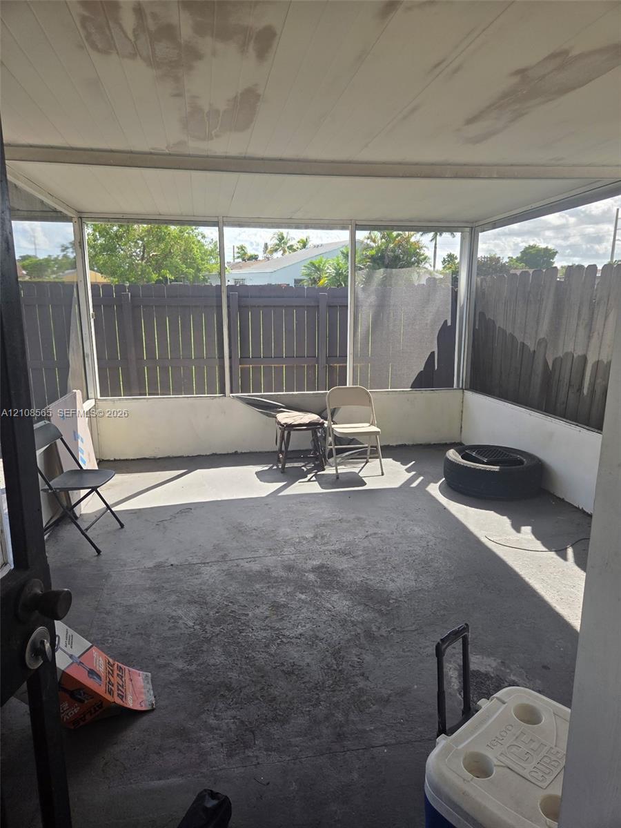 Enclosed porch featuring a concrete floor, screened-in walls, a solid roof, and a wooden privacy fence