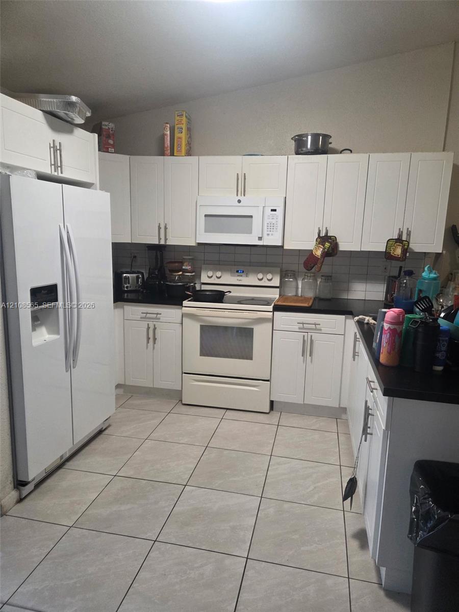 Kitchen featuring white shaker-style cabinetry, dark solid-surface countertops, white tile backsplash, and ceramic floor tiling