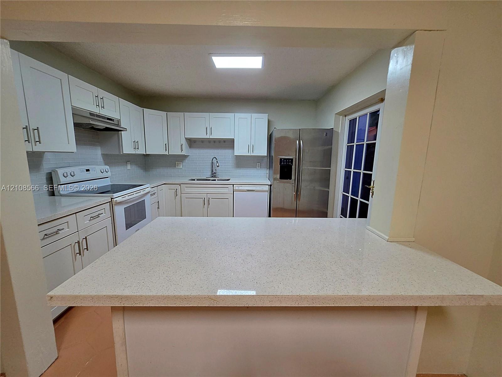 Kitchen featuring a peninsula with a quartz countertop, white cabinetry, a white subway tile backsplash, and stainless steel appliances