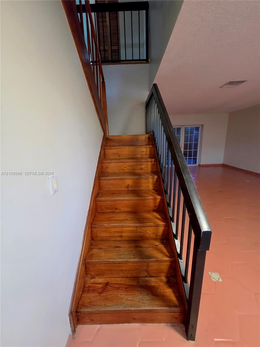 Staircase featuring natural wood treads, a wooden handrail, and dark metal balusters, complemented by tile flooring