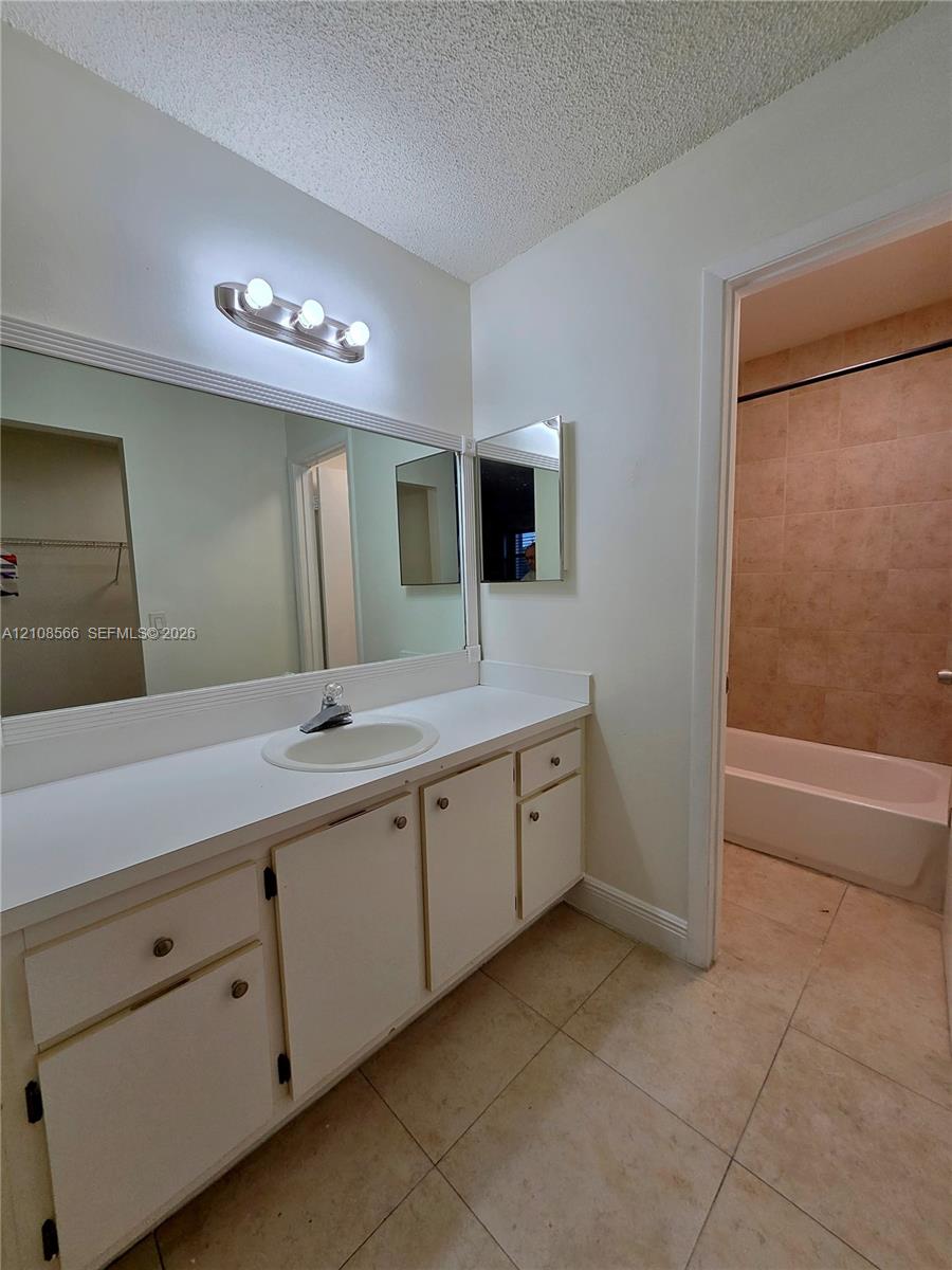 Bathroom featuring a wide vanity with white cabinetry, a large wall-mounted mirror, three-light fixture, and ceramic tile flooring, with a separate tub and shower enclosure tiled in neutral tones