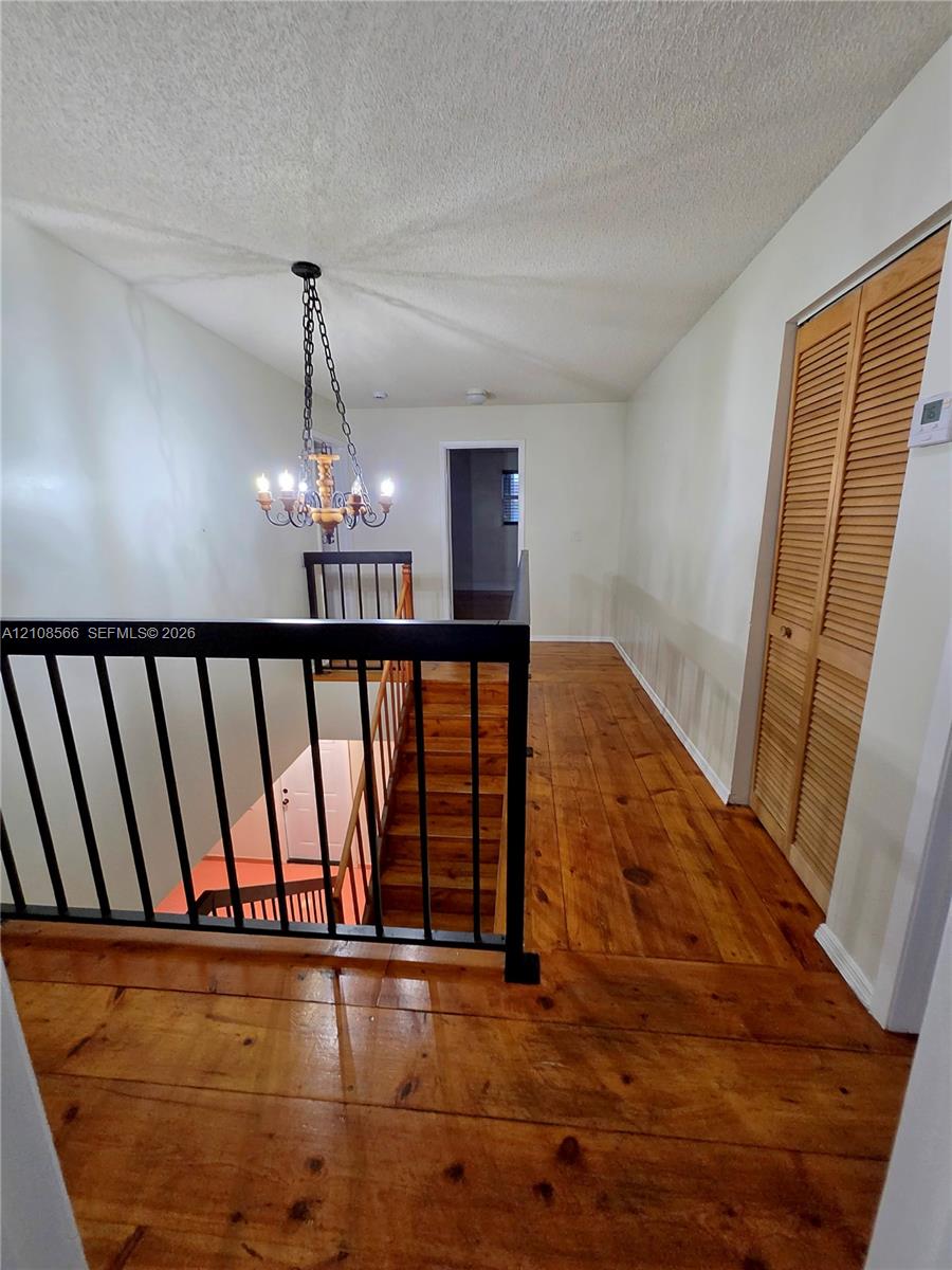 Staircase featuring wood-finish flooring, metal railing, louvered closet doors, and a multi-arm chandelier