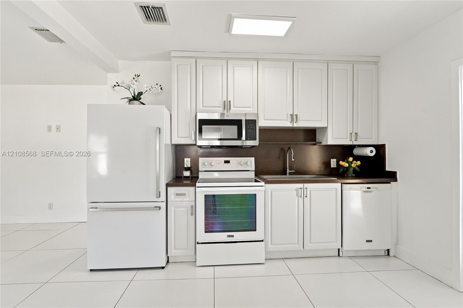Kitchen featuring white cabinetry, solid-surface countertops, integrated stainless steel microwave, large-format tile flooring, and stainless steel faucet hardware