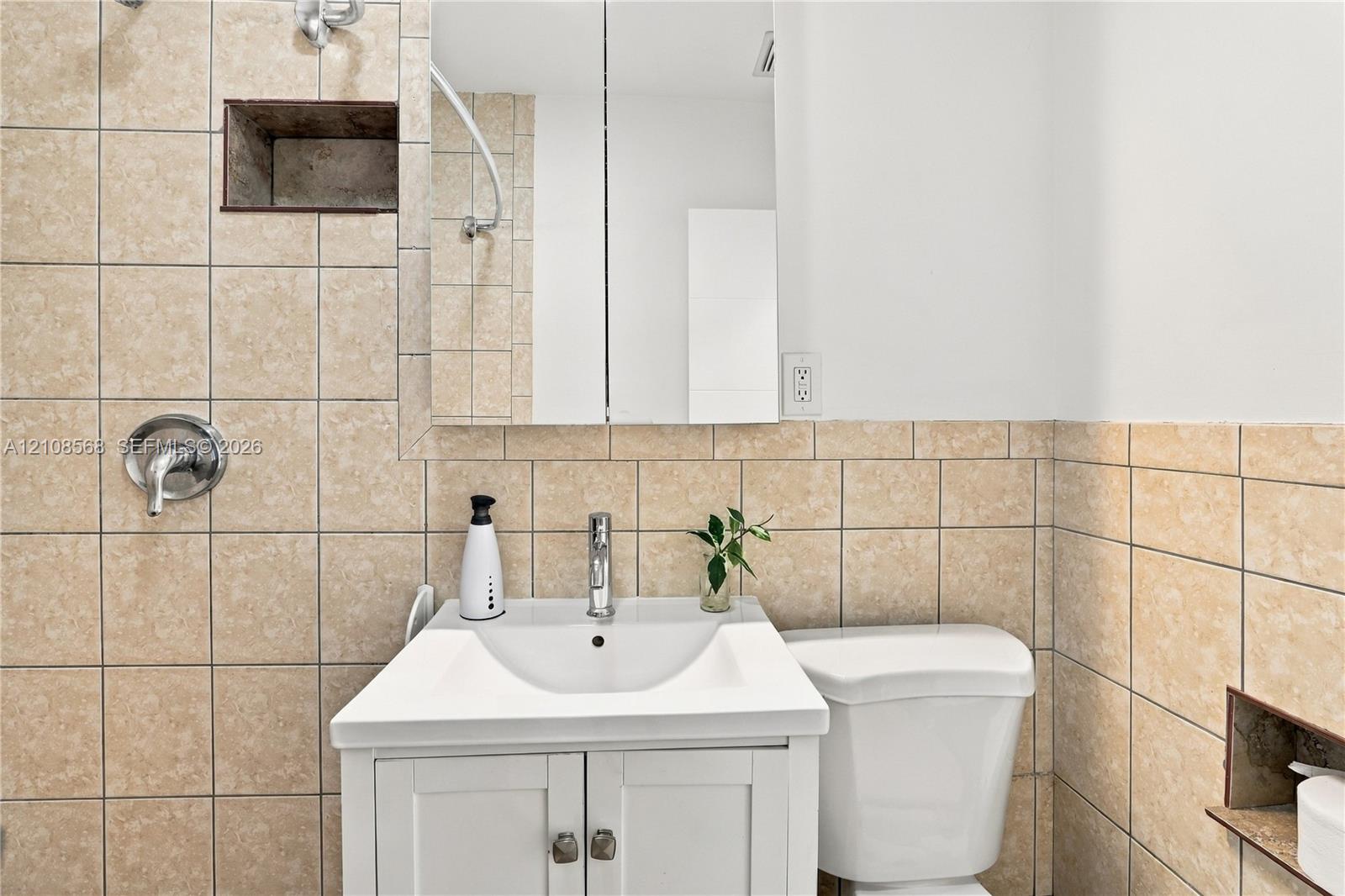 Bathroom featuring a white vanity cabinet with a ceramic sink, wall-mounted medicine cabinet with mirror, built-in wall recessed shelving, and tile wall surfacing