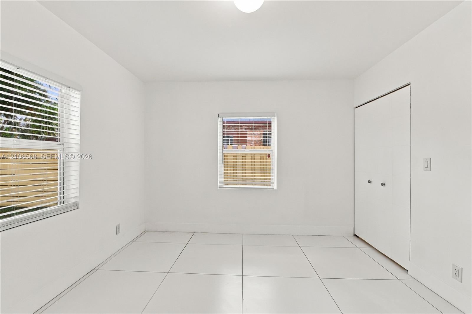 Neutral-toned interior room featuring large-format tile flooring, dual windows with fitted blinds, and a built-in double-door closet