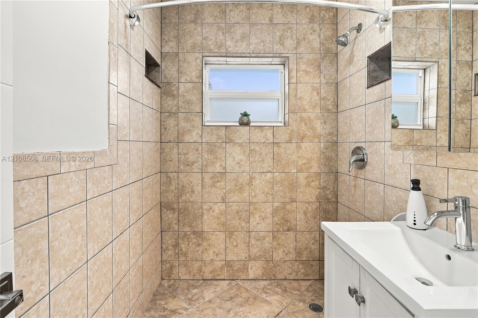 Shower area featuring stone-finish tile surround, built-in recessed wall niches, and a white vanity cabinet with a integrated sink and chrome faucet