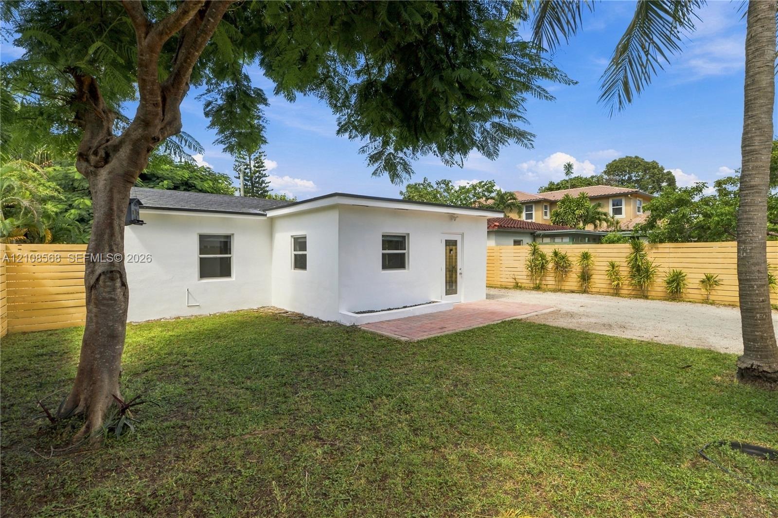 Backyard featuring a white stucco exterior, red brick patio, horizontal wood fencing, and mature trees