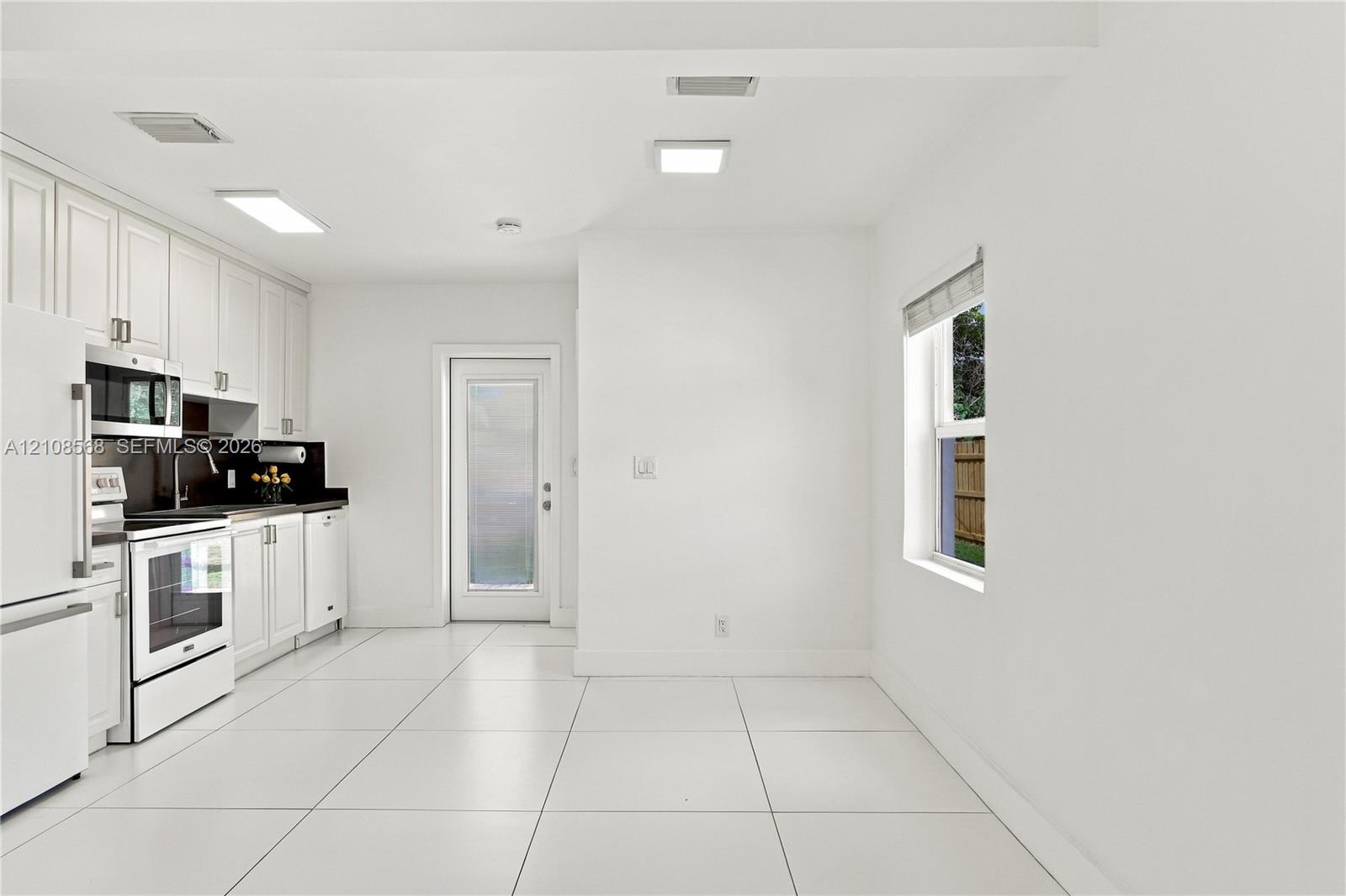 Kitchen featuring white shaker-style cabinetry, dark stone-finish countertops, tile flooring, and integrated white appliances