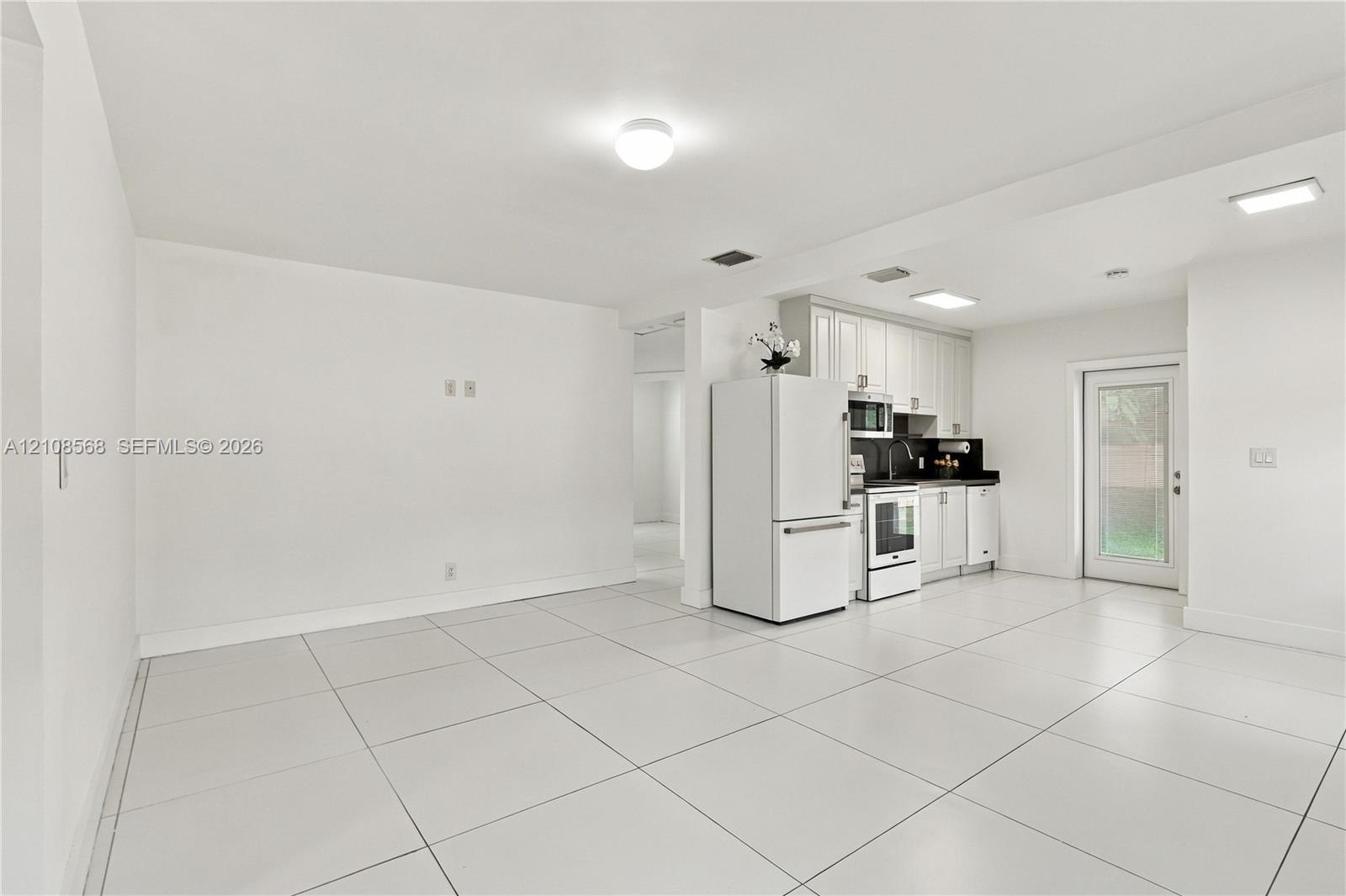 Open floor plan featuring large-format ceramic tile flooring, white shaker-style cabinetry, a glass-paneled exterior door, and recessed lighting