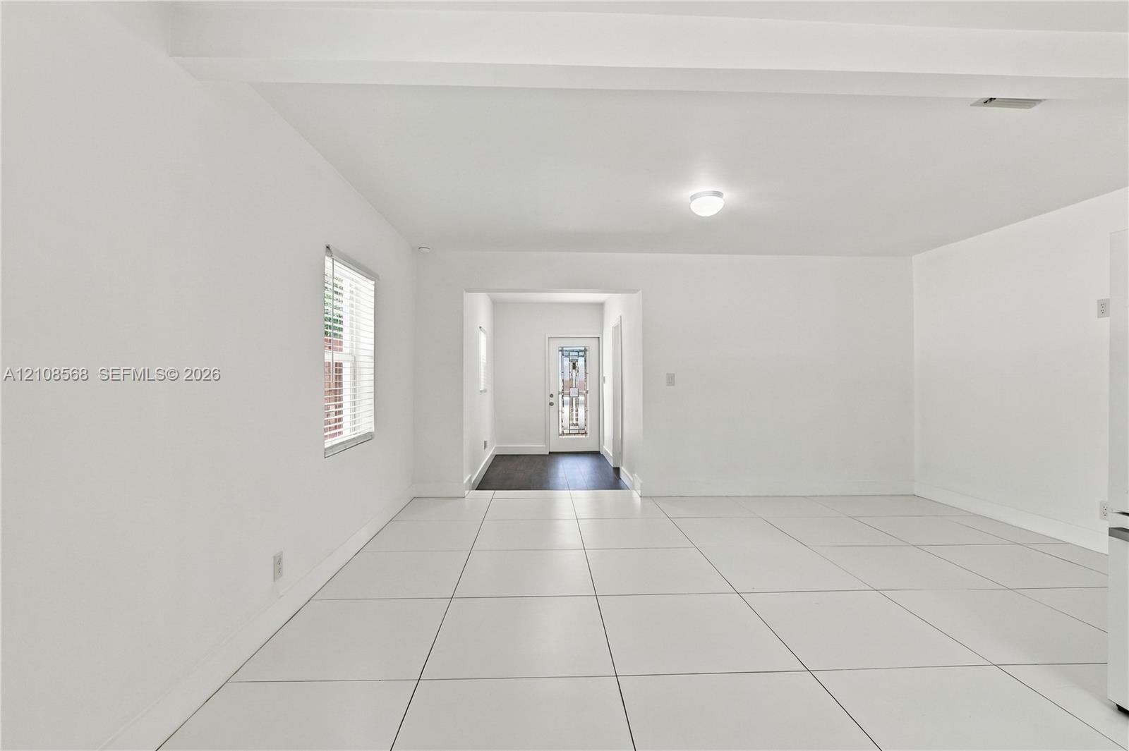 Large-format white tile flooring, ceiling beam detail, white wall finishes, and exterior door with glass detailing