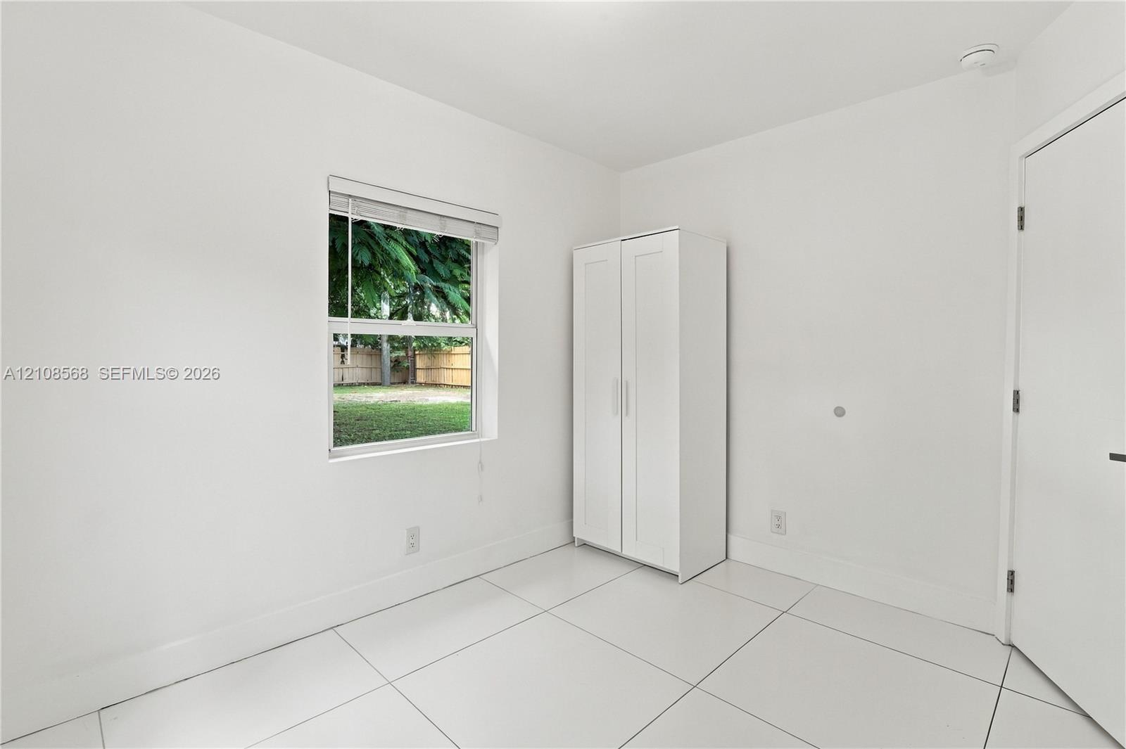 Neutral interior space featuring polished white tile flooring, crisp white walls, and a single-pane window with a white horizontal blind